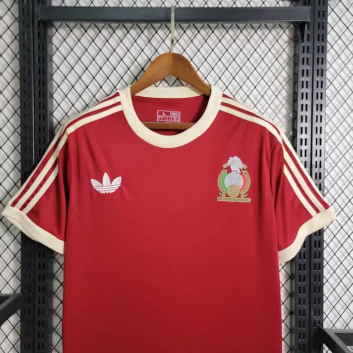 01290c0d47af65bd_70485846-6c55-4669-b7a4-87aba331820f | AE JERSEY Red Adidas sports jersey on a hanger with white stripes on the shoulders and cream cuffs; crest on the left chest and white Adidas logo on the right.