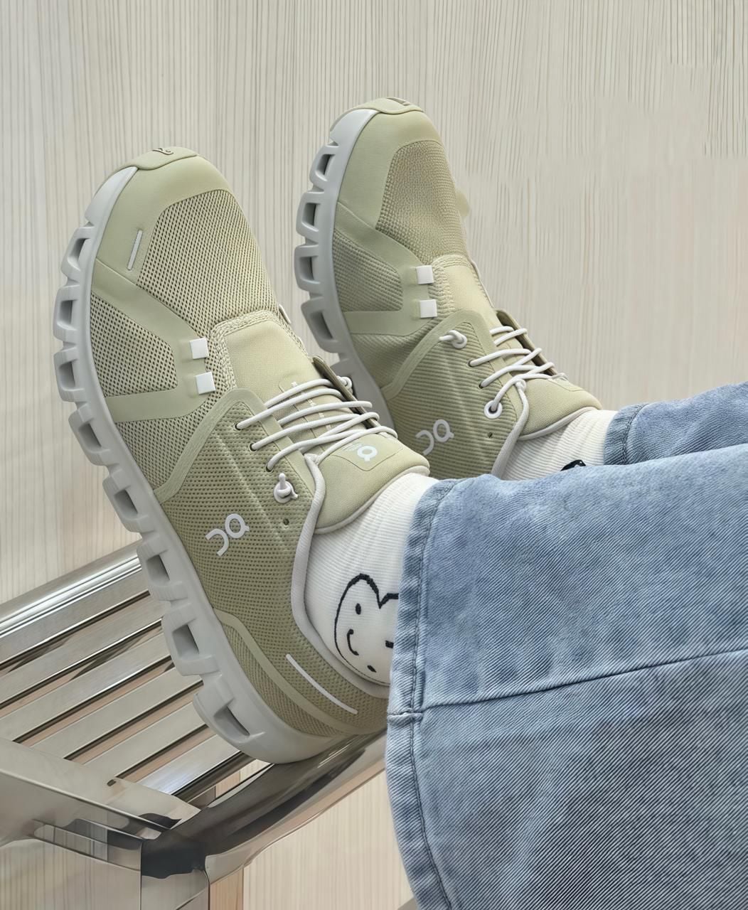028bbc75-4688-40c1-a85c-2f929a0064f6 | AE JERSEY Beige athletic sneakers with chunky gray soles, white laces, worn with light-wash jeans and socks featuring a smiley face.