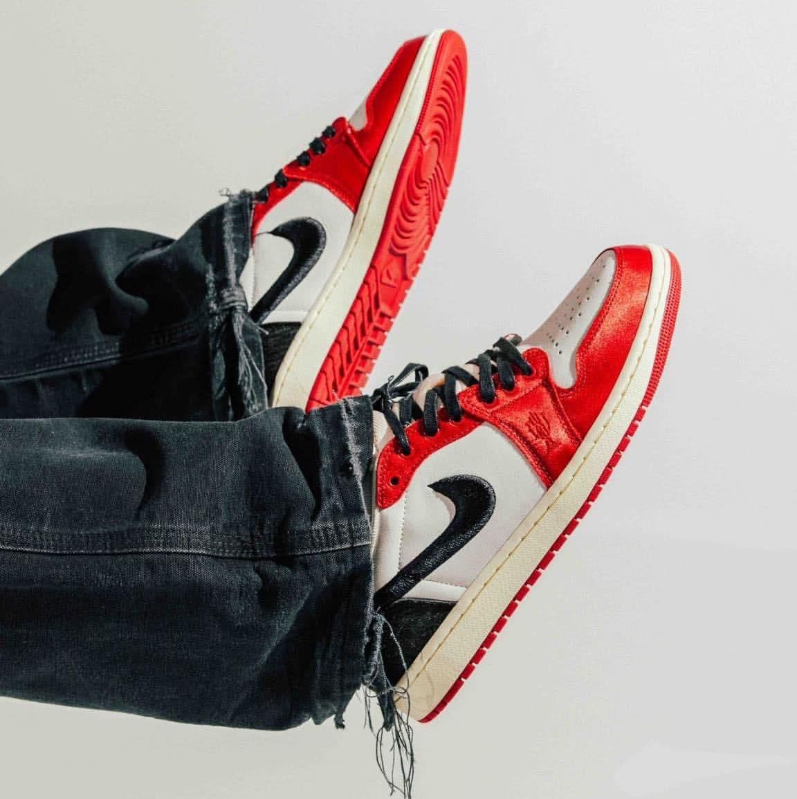 0386fcd5-68f4-47d3-b717-2d69f3e5177d | AE JERSEY Red and white sneakers with black laces and a black swoosh, paired with cuffed dark jeans against a light background.