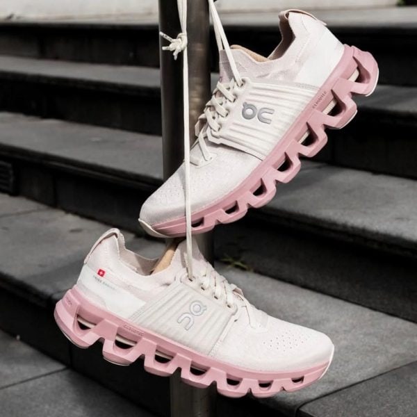White sneakers with pink soles hanging from a metal pole on concrete stairs beside a railing.