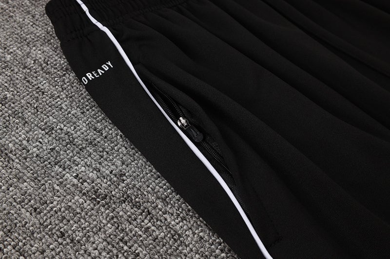 0807c6c9 | AE JERSEY Close-up of black athletic pants with white piping and a zipper pocket on a gray carpet.