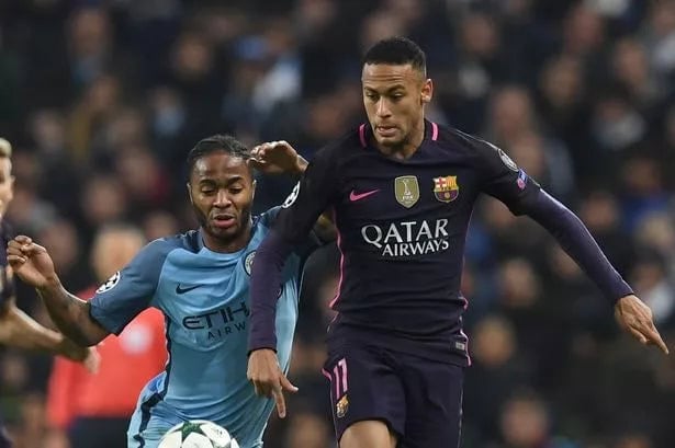 0_GettyImages-620133208 | AE JERSEY Two footballers chase the ball during a match, one in Barcelona’s dark purple kit and the other in Manchester City’s light blue kit.