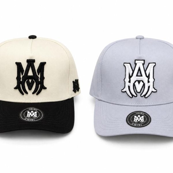 Two baseball caps displayed side by side: a beige crown with a black brim on the left and a light blue crown with a matching brim on the right, each with a bold M logo on the front and an M on the side panel.