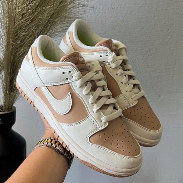 Beige and white Nike sneakers being held up, showing a perforated toe box and white laces.