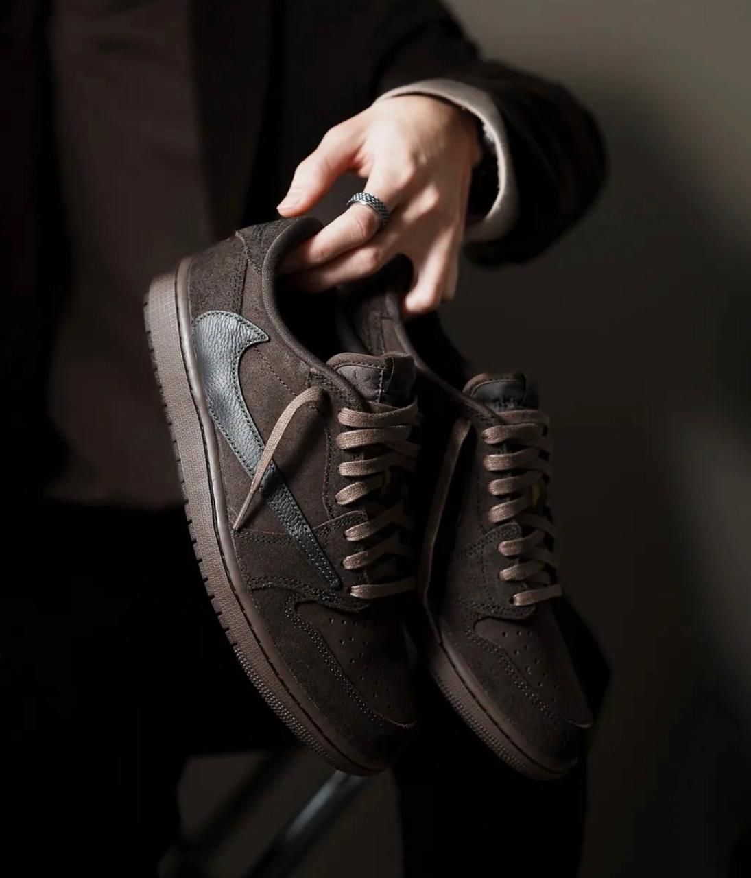 101410ae-0034-4d48-9ef8-8d6e23475717 | AE JERSEY Brown suede sneakers with blue side panels are being held by a hand wearing a silver ring.