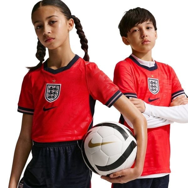 Two young soccer players in red England jerseys pose with a soccer ball between them, white background.