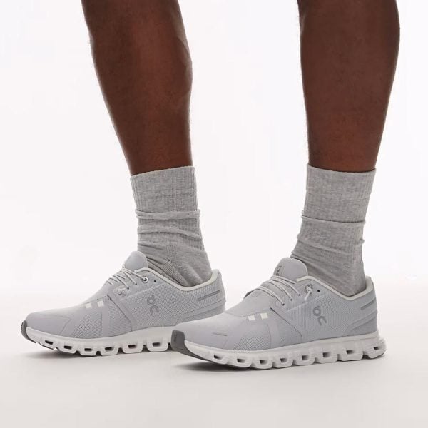 Light gray running shoes with thick white soles worn with gray crew socks, standing on a white background.