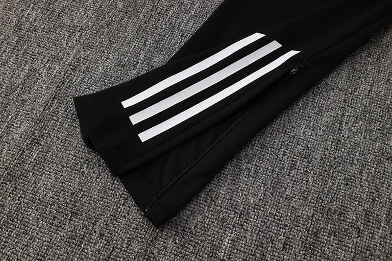 13deac29 | AE JERSEY Black athletic pants with three white stripes along the leg and a zip at the ankle on a gray carpeted floor