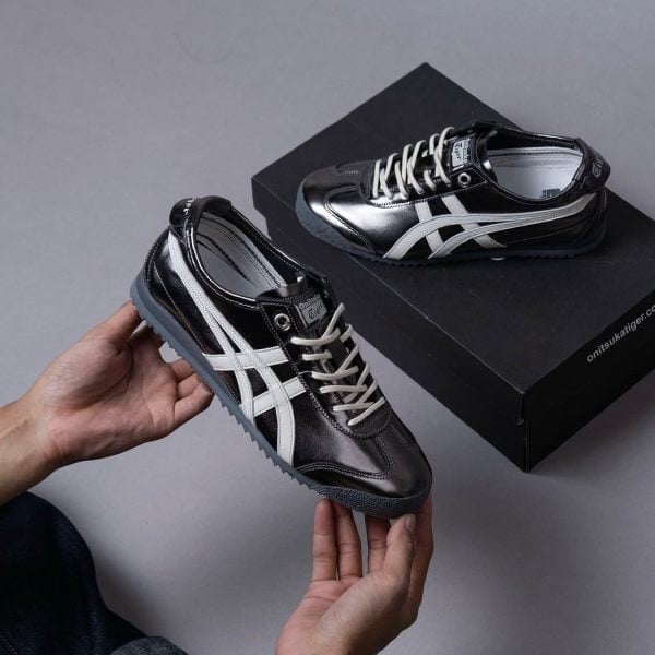Pair of black Onitsuka Tiger sneakers with white stripes, one held in hand and one resting on a black shoe box.