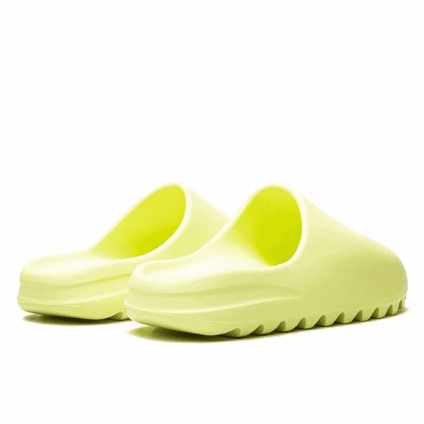 Close-up of lime-green slip-on sandals with wide, curved straps on a white background.