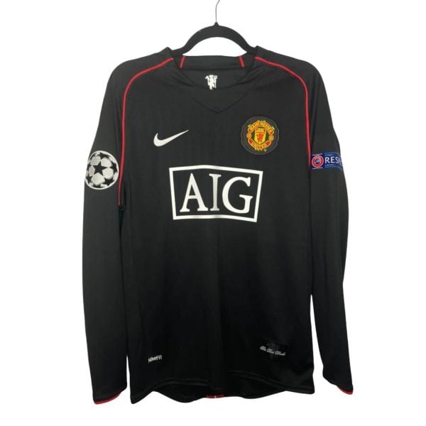 Manchester United black jersey on a hanger, with AIG sponsor, Nike swoosh, club crest, and Champions League patch on the sleeve.