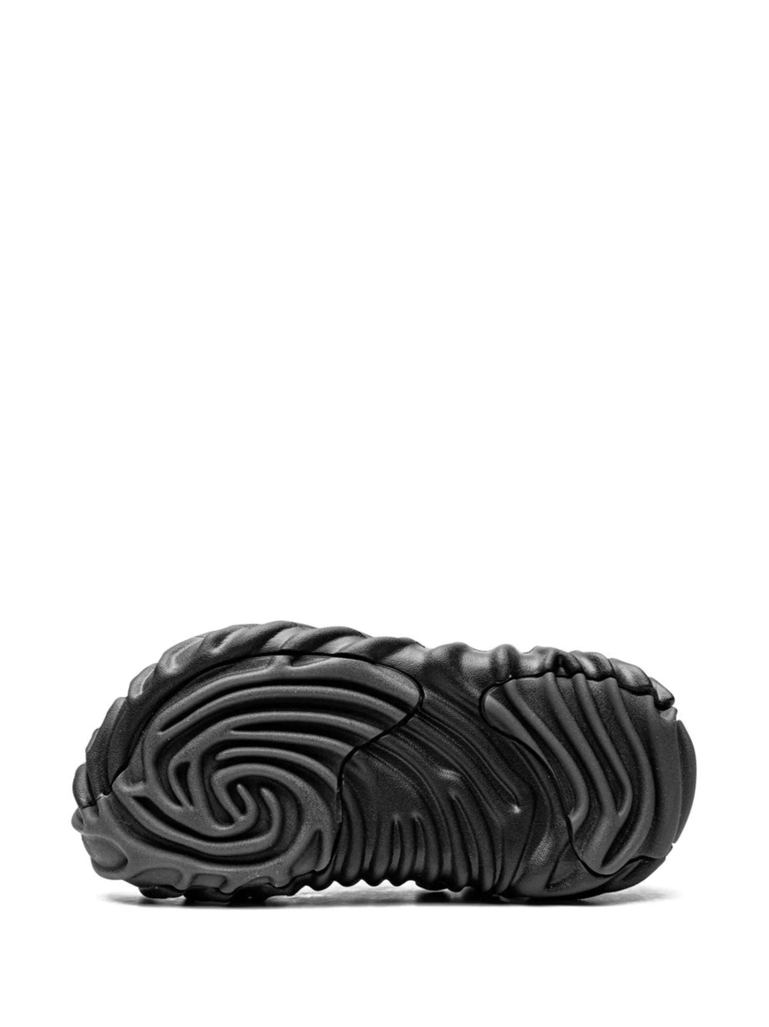 19201488_42050654_2048 | AE JERSEY Close-up of a black sneaker sole with curved, ribbed tread patterns on a white background
