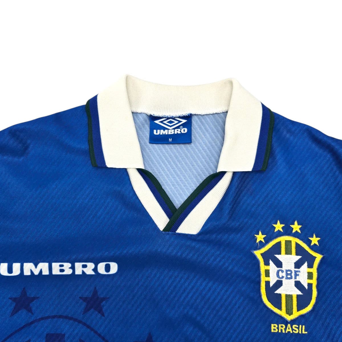 199394-brazil-away-football-shirt-m-umbro-ff204564-624925 | AE JERSEY Blue Brazil national team jersey close-up showing white collar, Umbro branding, and the CBF crest with a yellow shield and blue background.