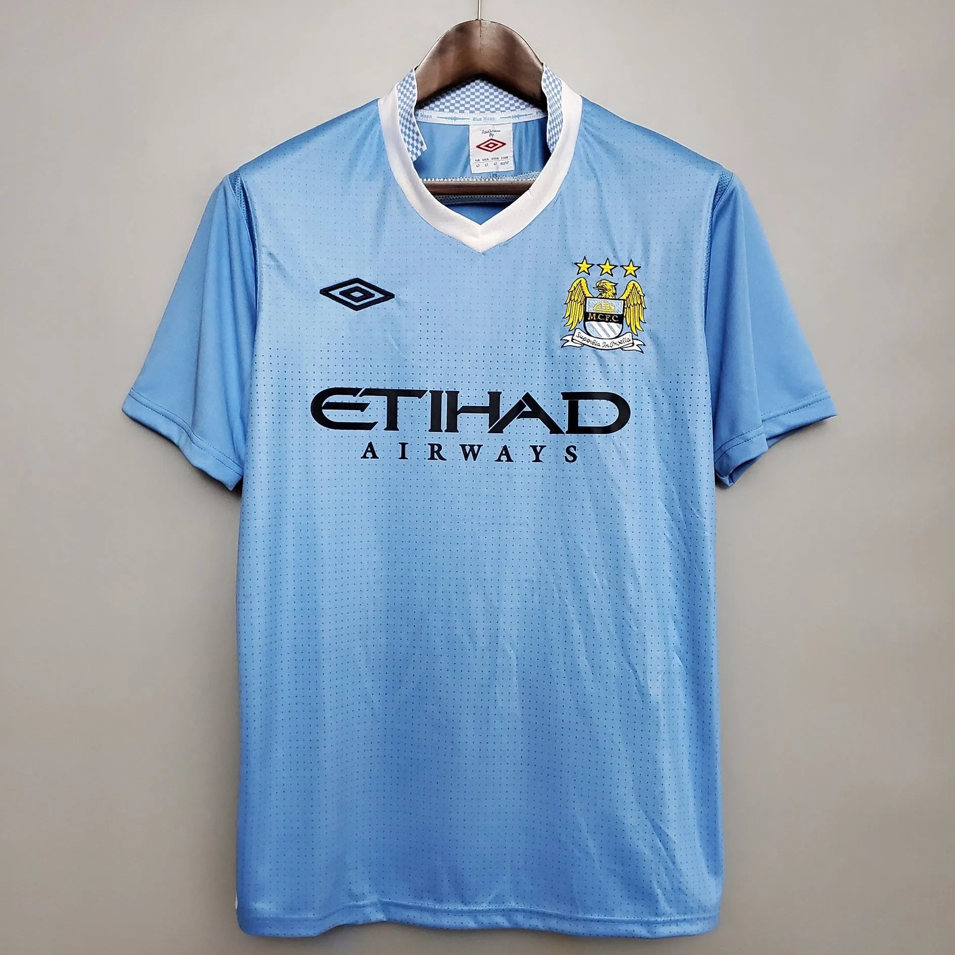2012-Manchester-City-Retro-Home-Short-Sleeve-Jersey1-e1657183218423 | AE JERSEY Light blue Manchester City jersey on a hanger, showing club crest with three stars and the ETIHAD AIRWAYS sponsor.