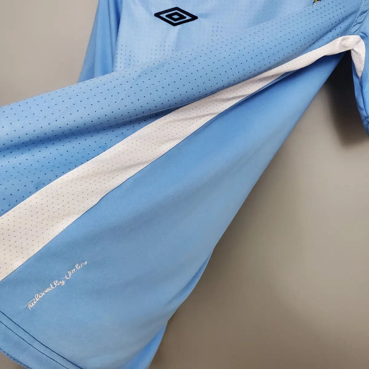 2012-Manchester-City-Retro-Home-Short-Sleeve-Jersey7 | AE JERSEY Light blue perforated sports jersey sleeve with a white stripe and the Umbro diamond logo on the shoulder area.