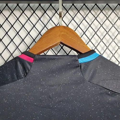 20903b_732b1936e6ce4f68bffa621a19c7b137_mv2 | AE JERSEY Back view of a dark gray speckled athletic shirt with pink and blue collar accents on a wooden hanger against a metal grid wall.