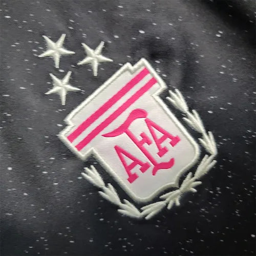 20903b_8c691911039443fcb1bc9fa0e8306d22_mv2 | AE JERSEY Close-up of a white shield patch with pink ALA letters, pink stripes, and a laurel border on a dark speckled fabric background.