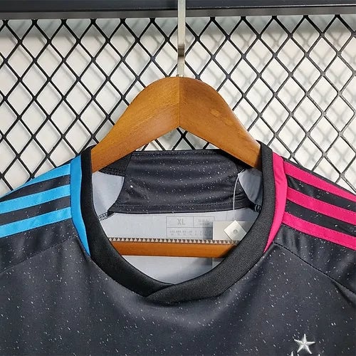 20903b_912a5b0f79e449dda7f4f6606a02e941_mv2 | AE JERSEY Black athletic jersey on a wooden hanger with blue shoulder stripes on the left and pink stripes on the right, size XL, against a metal grid backdrop, with a small star emblem visible.