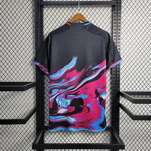 20903b_96a1a3e6a43d40f0b59b0e5baa2daa22_mv2 | AE JERSEY Black T-shirt with bright pink, blue, and cyan abstract swirl pattern on the back, hanging on a wooden hanger in a metal display rack