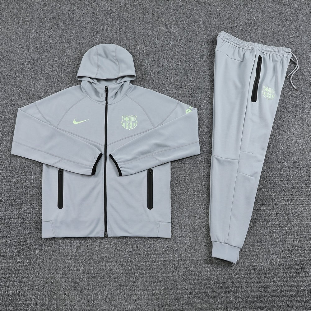 224e6094 | AE JERSEY Light gray Nike Barcelona training jacket with a hood and neon crest, paired with matching jogger pants laid flat on a gray carpet.