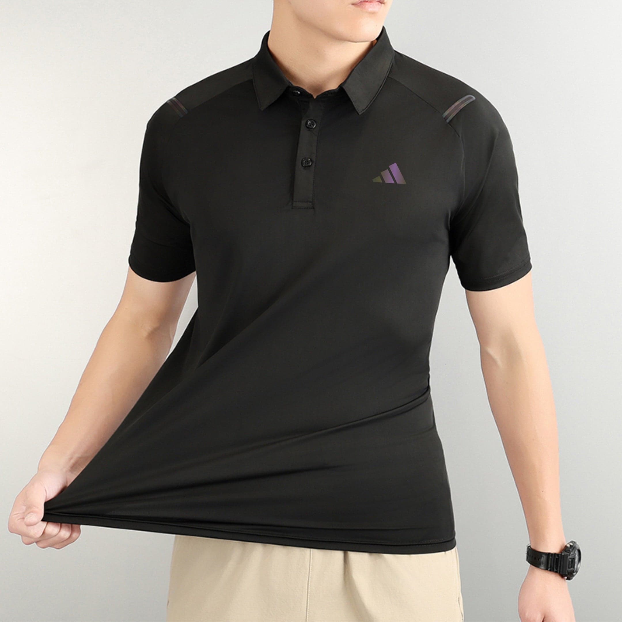 2647552d | AE JERSEY Person wearing a black polo shirt with a small purple triangle logo on the chest, beige shorts, and a black wristwatch visible on the right wrist.