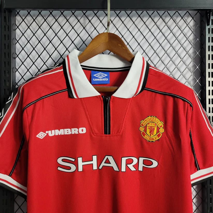 2_75bf0fac-6e08-4569-899b-7a974517c282 | AE JERSEY Red Manchester United football jersey on a wooden hanger, featuring the Umbro logo, club crest, and SHARP sponsor text.