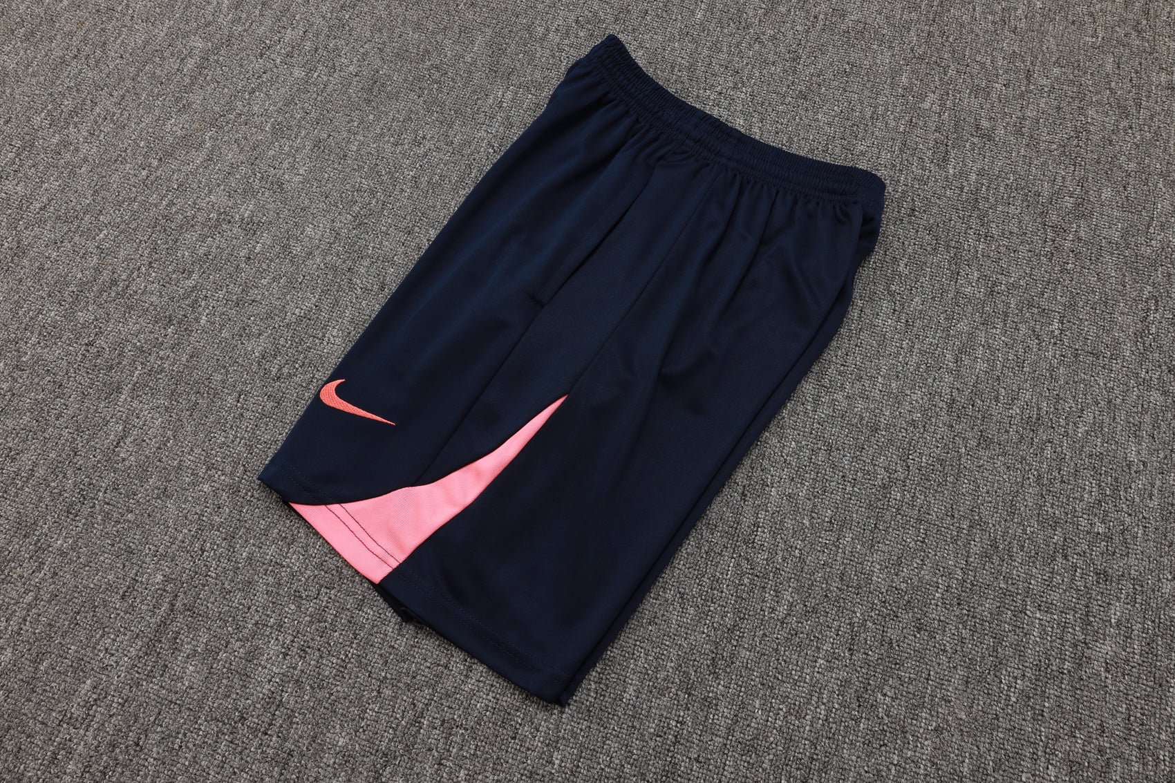 2cd95220 | AE JERSEY Navy athletic shorts with a pink Nike swoosh and pink panel on the leg, laid on a gray carpet.