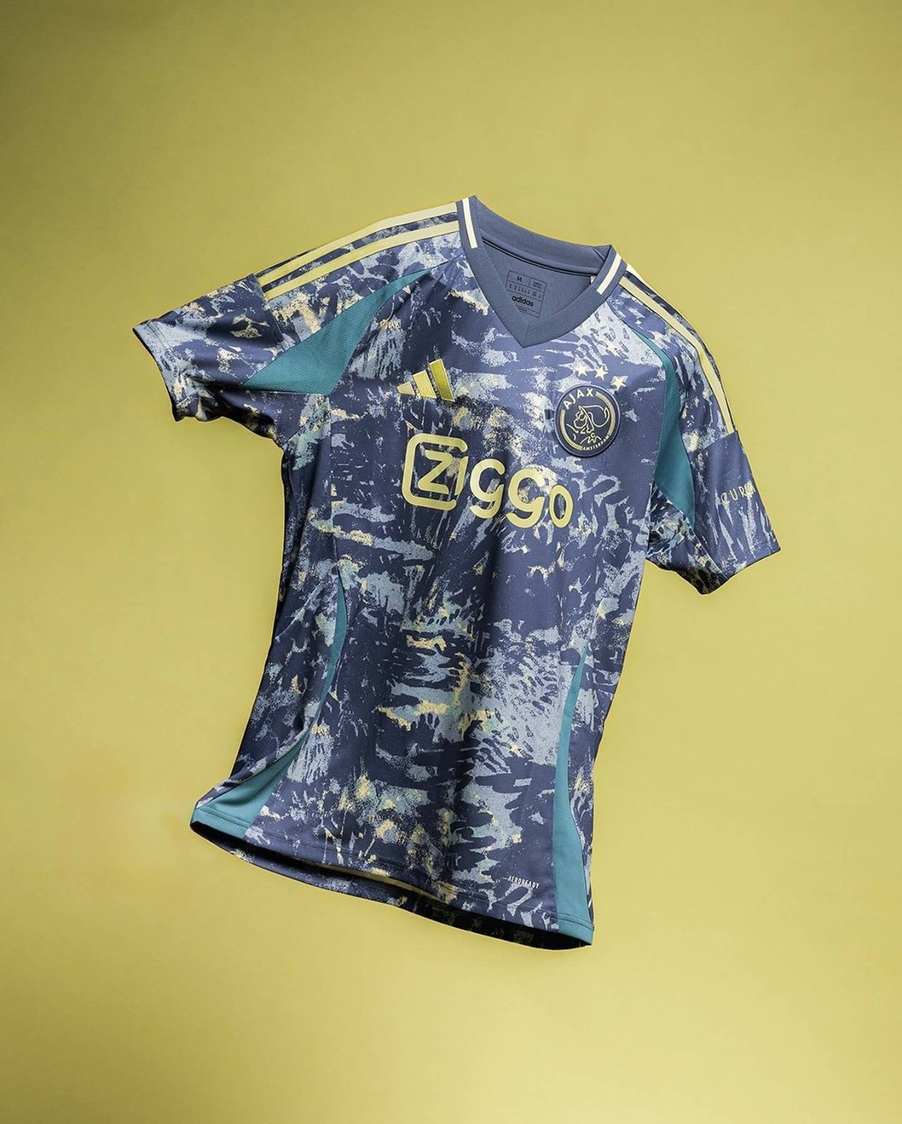 2wPdRtVJBjpaRvk | AE JERSEY Ajax football jersey with blue camouflage pattern, yellow Ziggo logo, and Adidas stripes on shoulders against a yellow backdrop