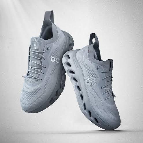 Two gray On running shoes shown midair, side and top views with breathable knit uppers and distinctive cloud sole pods.