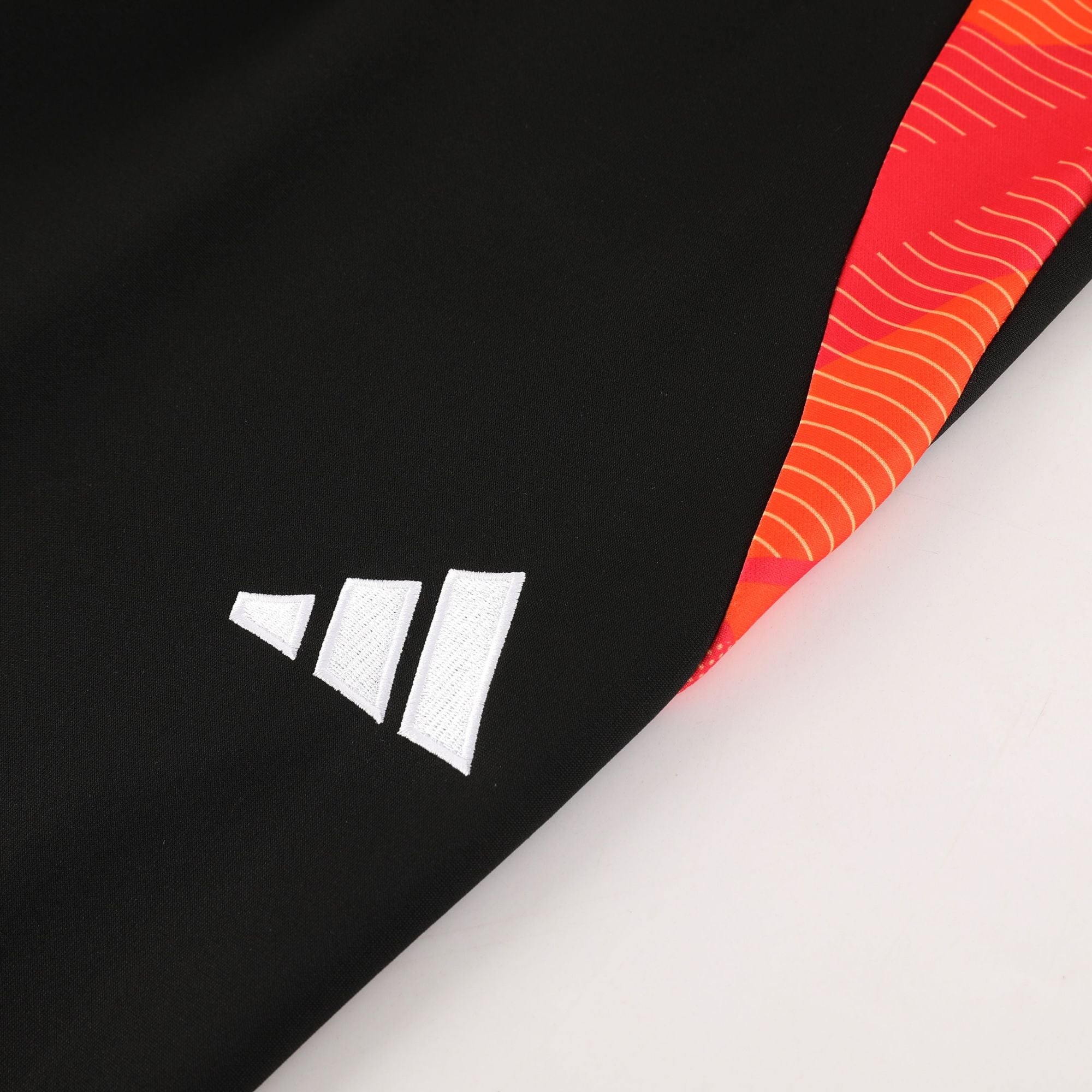 31307c71 | AE JERSEY Close-up of black fabric with white stitched rectangular patches and an orange patterned trim along the edge.