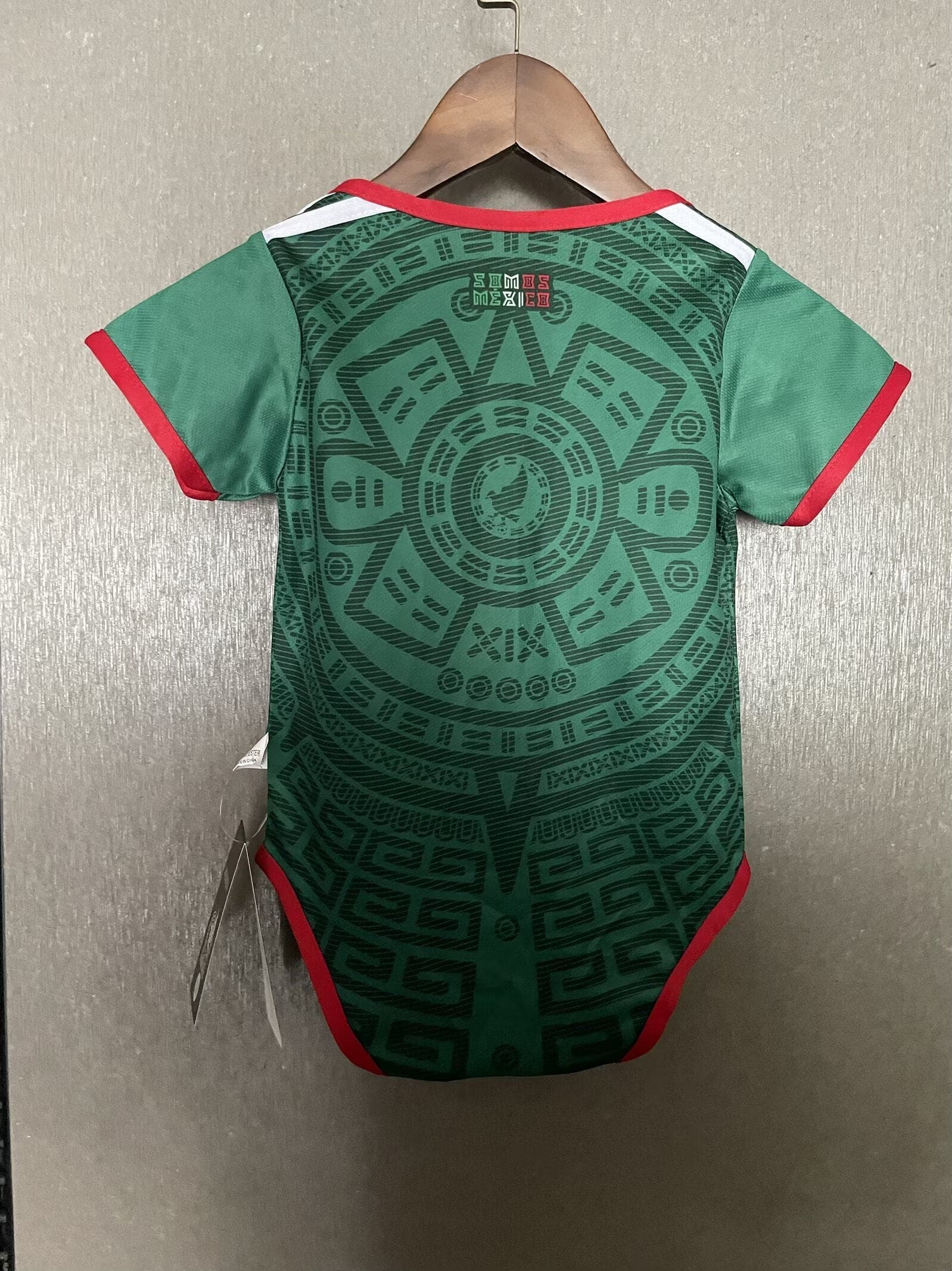 32224290 | AE JERSEY Green t-shirt on hanger, red trim at neck and sleeves, showing an intricate geometric pattern on the back.