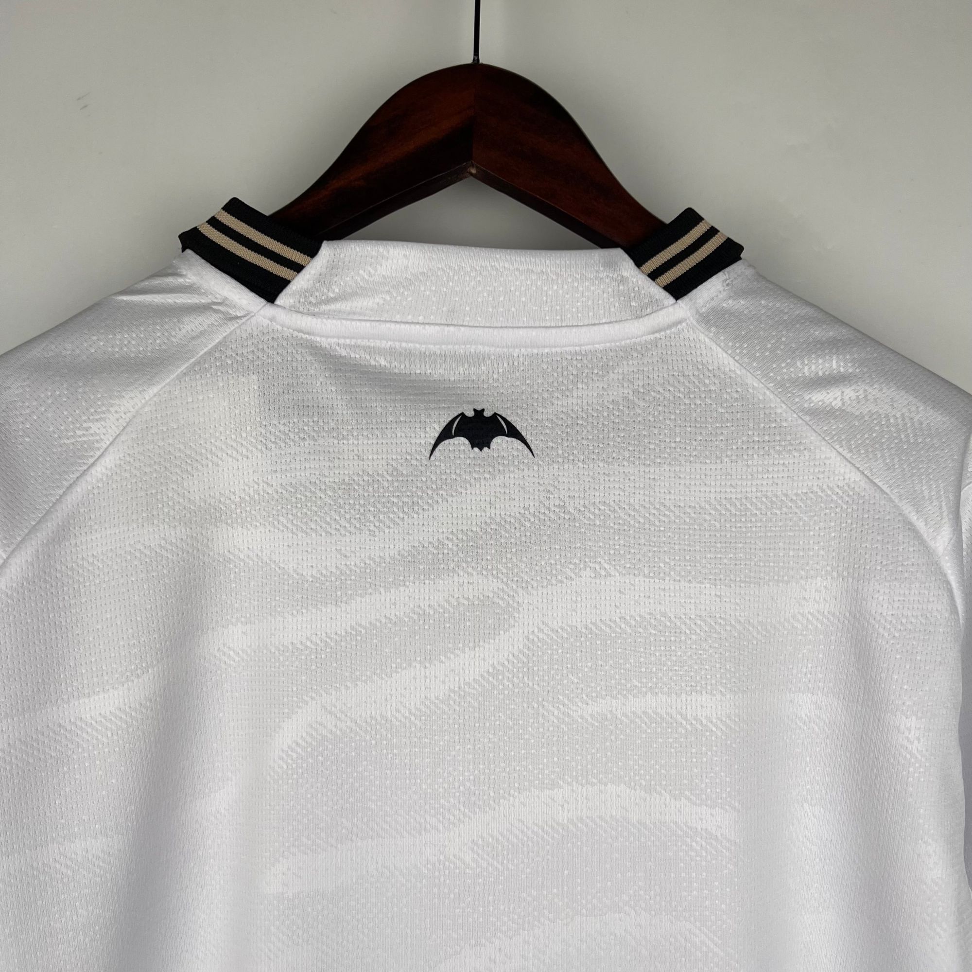 327f9fb3_54a80eec-2688-4d99-b1af-ec0fce1b4b2b | AE JERSEY White polo shirt on a wooden hanger with a Batman logo on the chest.