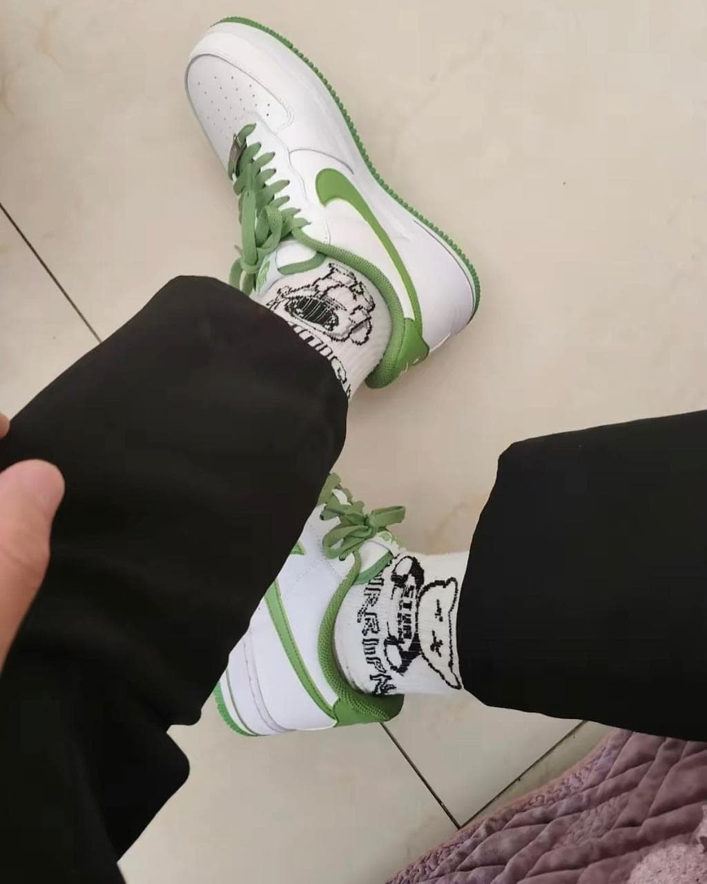 369e9ef1-19cf-4a82-aaf9-63bfce2fb3bd_68ff5489-4e72-4f10-afd1-a8af291c6eb7 | AE JERSEY Top-down view of a person wearing white and green sneakers with green laces, black pants, and white socks with a panda graphic.