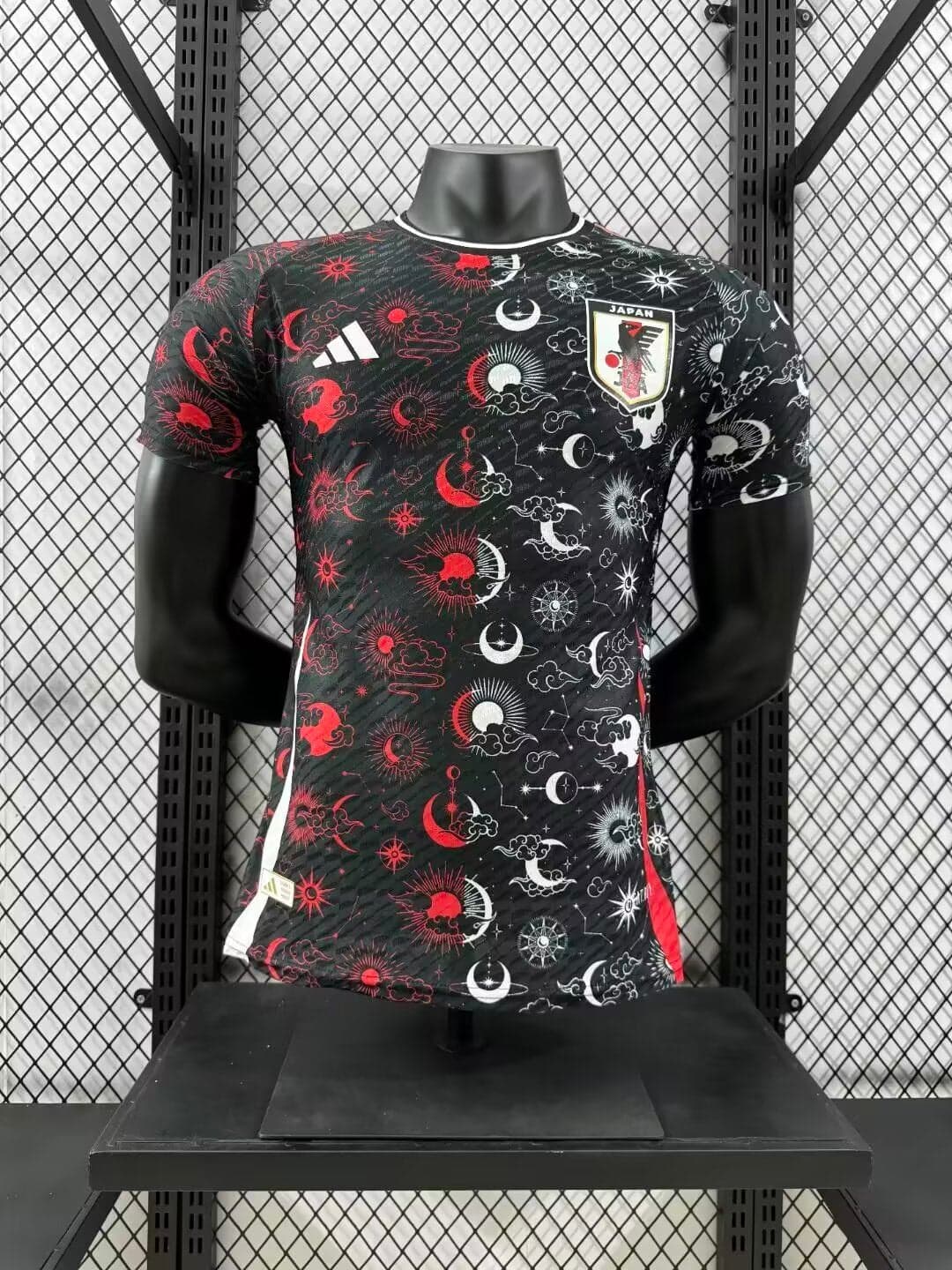 37a6b296 | AE JERSEY Mannequin wearing Japan national team jersey with black celestial print, containing red and white suns and moons, crest on chest, Adidas logo on the right.