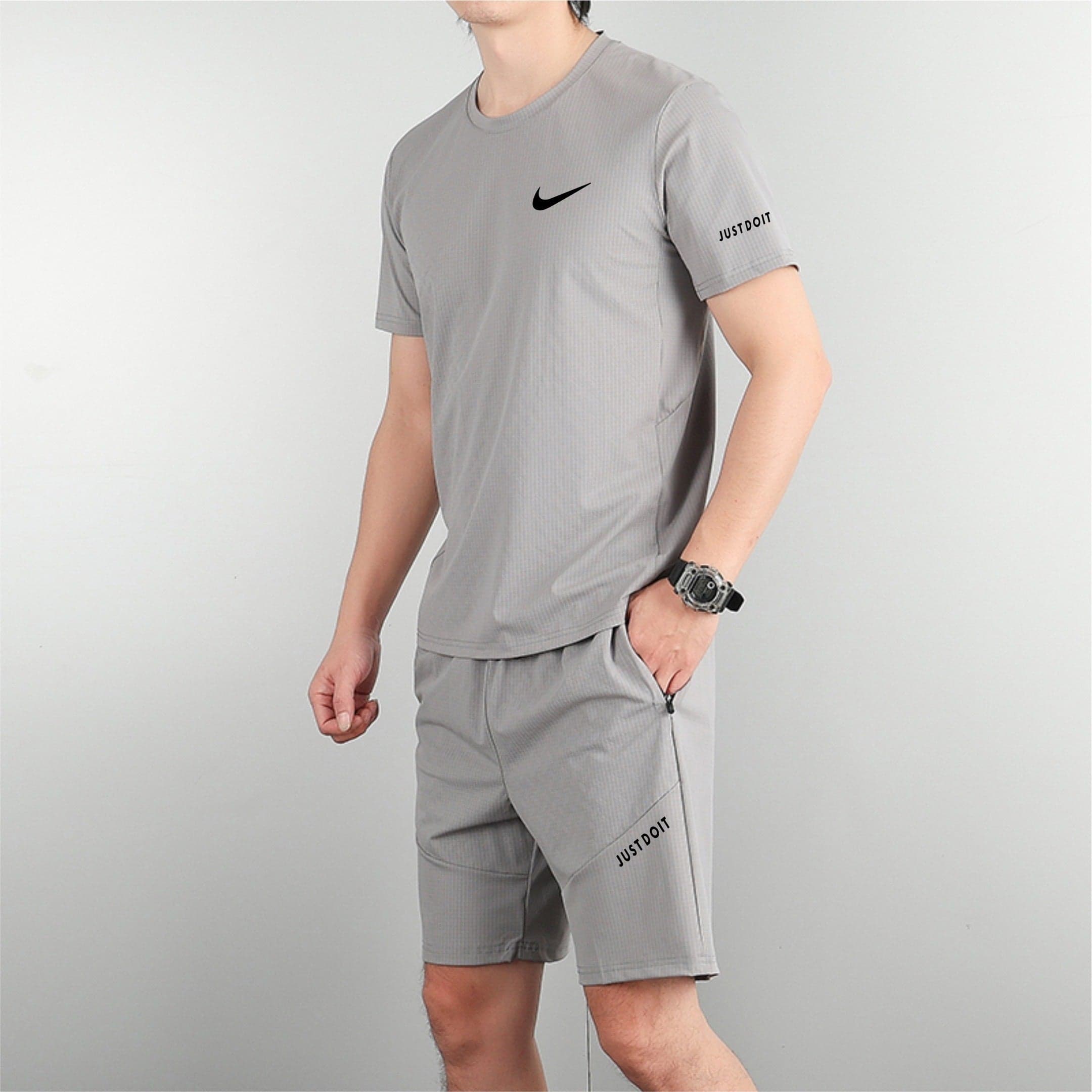 3999a757 | AE JERSEY Man wearing a light gray athletic shirt with a black Nike swoosh on the chest and 'Just Do It' text visible on the sleeve/short leg edge, standing sideways with a watch on the wrist.