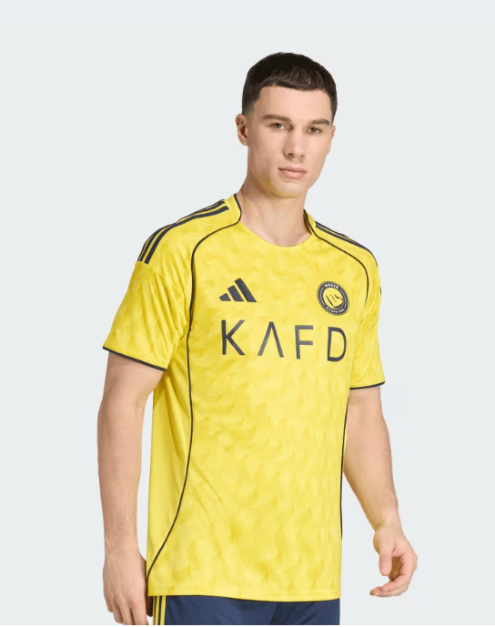 3A | AE JERSEY Male model wearing a bright yellow Adidas soccer jersey with a circular team crest and the letters KAFD across the chest.