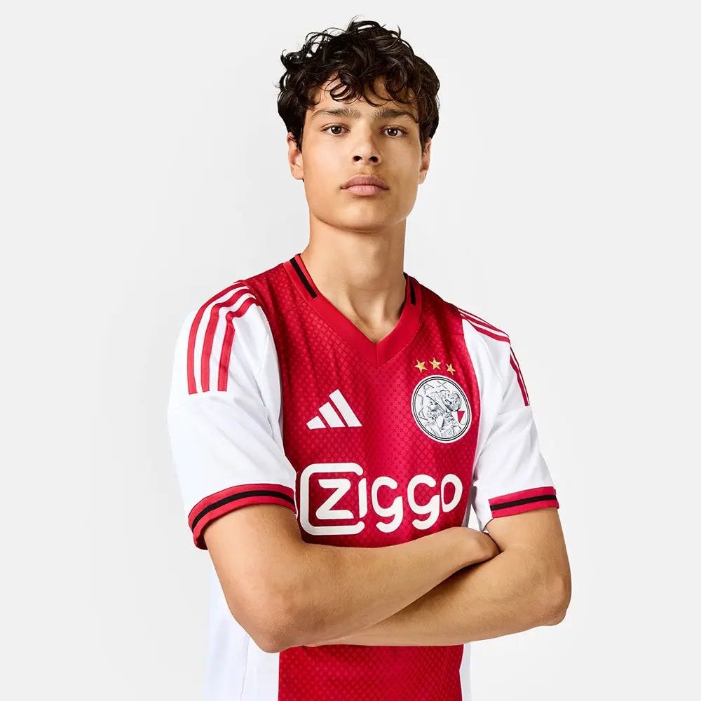 3cbc4bb9-e3b1-e22e-29aa-c3a75b27344c | AE JERSEY Young male soccer player standing with arms crossed, wearing a red and white jersey with Ziggo sponsor and team crest visible.
