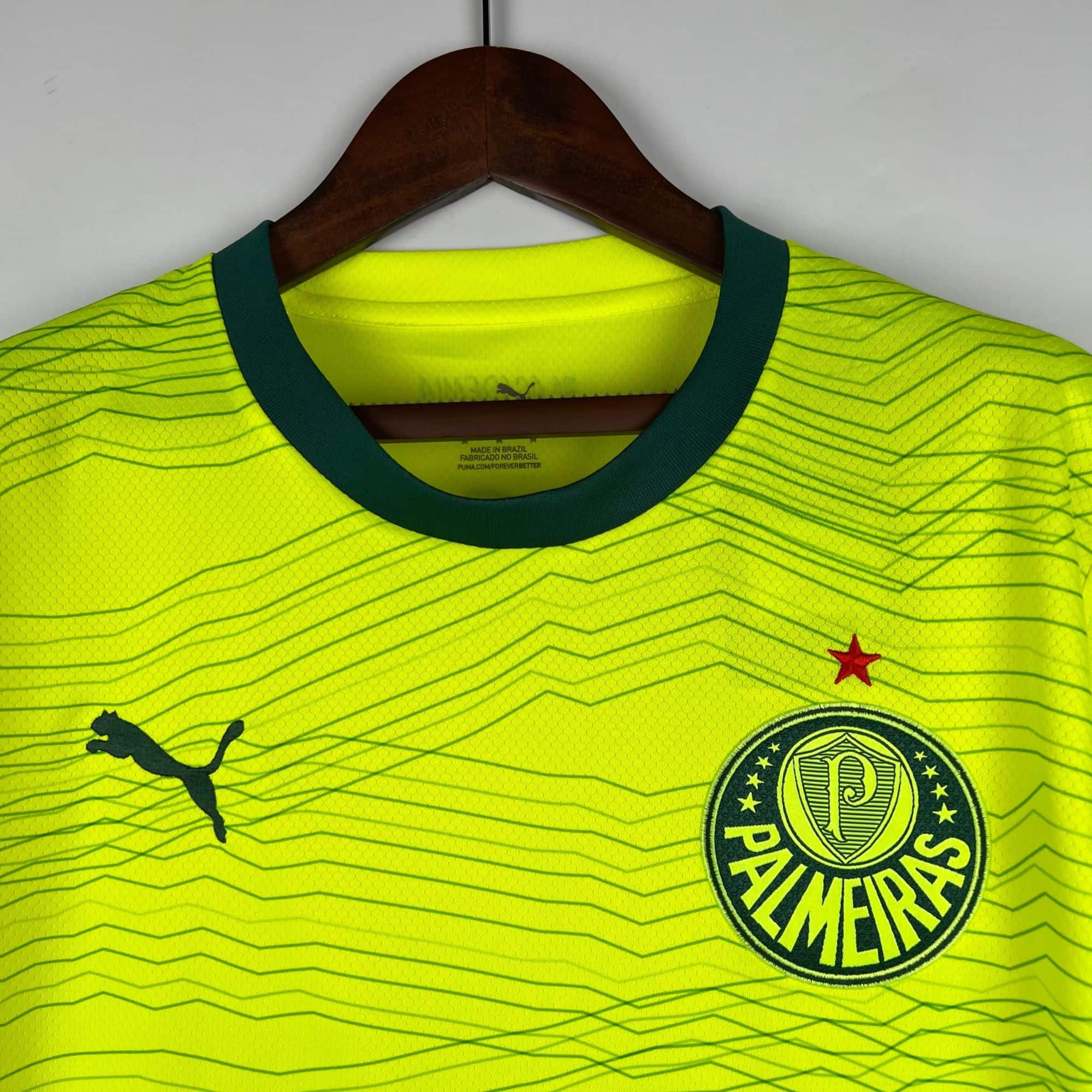 3f01d108_6ea5d9a7-3ab8-45a3-9622-2113ae277862 | AE JERSEY Neon yellow athletic jersey on a wooden hanger with a dark green collar, featuring a round crest at the lower right and a Puma logo nearby.