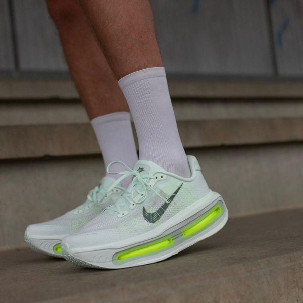 White Nike running shoes with neon green air-cushioned soles, worn with white socks on a concrete step backdrop.