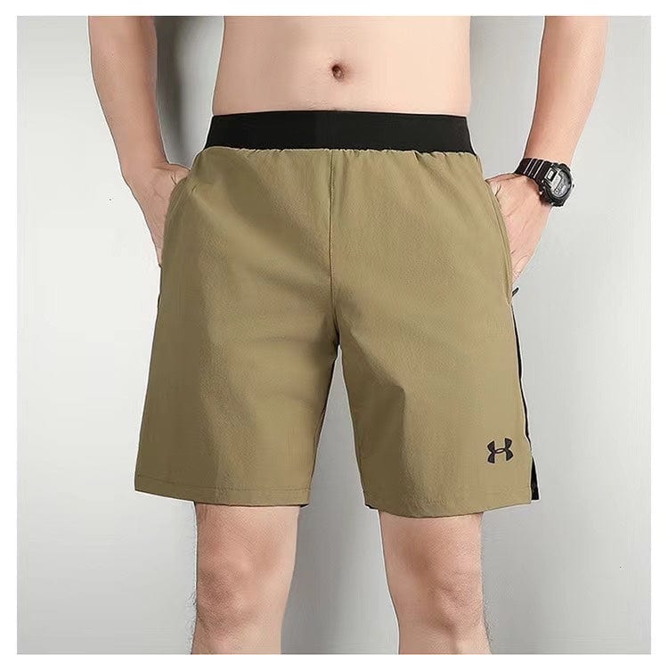 3f2c1dac | AE JERSEY Man wearing tan athletic shorts with a black waistband; Under Armour logo on the left leg, hands in pockets, watch on left wrist.