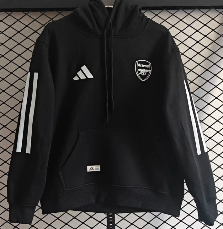 3f7be656-3552-4838-9bc3-d9b1bbcab149 | AE JERSEY Black Arsenal hoodie with Adidas logo and crest, long sleeves with white stripes, front pocket, hanging against a chain-link background.