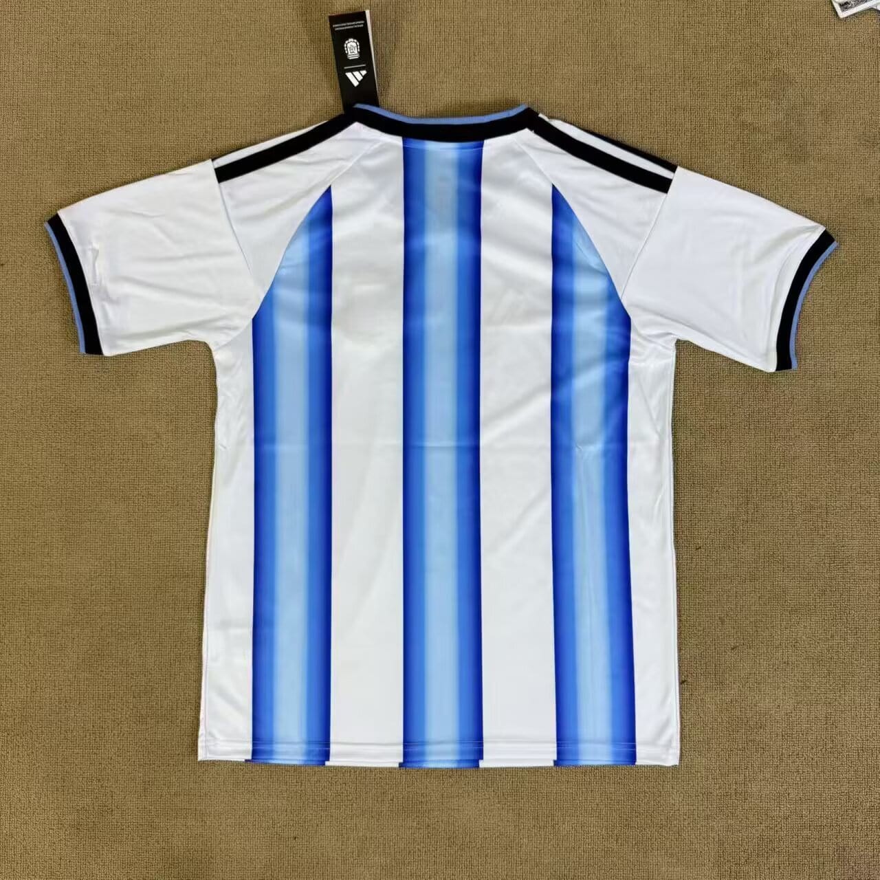 41a3ffec | AE JERSEY Back view of a white soccer jersey featuring bold vertical blue stripes, with black trim on the collar and sleeves and a tag attached at the neck edge.