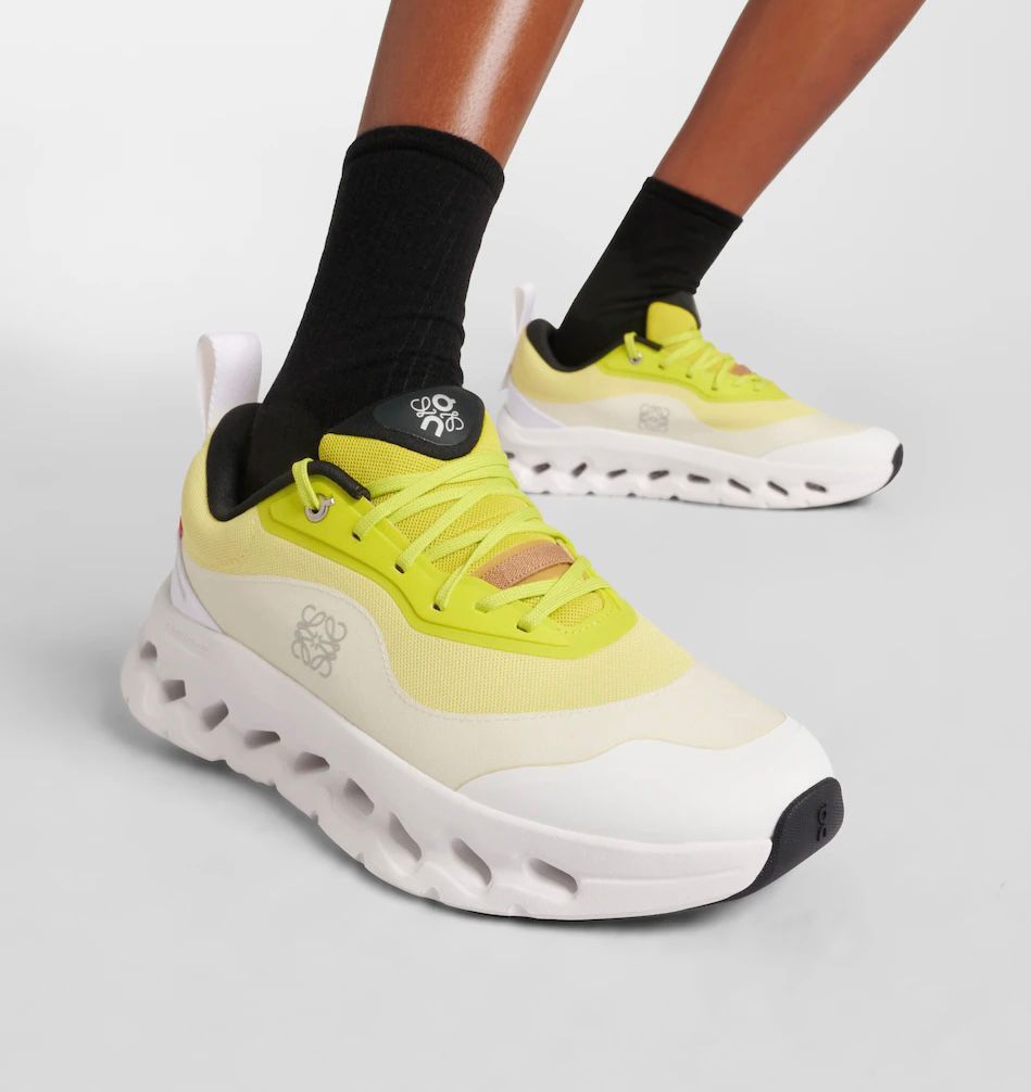 43af550d-c302-46e9-885d-447d33f92e7d | AE JERSEY Bright yellow chunky sneakers with white thick sole on a model wearing black socks, close-up view of one foot in front of the other on a gray background