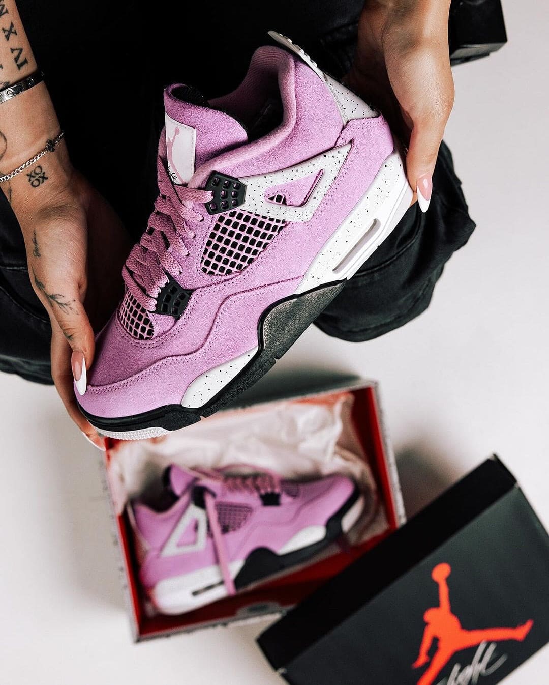 464467477_18379793371096448_6068591995547629227_n | AE JERSEY Close-up of a pink and white Air Jordan sneaker being held, with another pink pair inside a red Jordan box nearby.