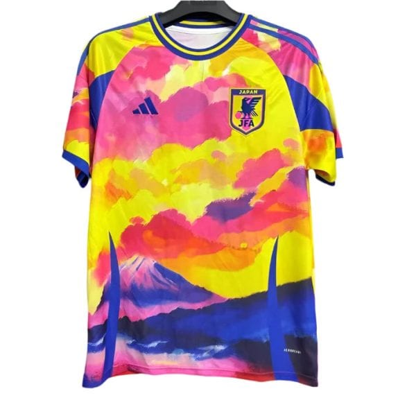 Colorful Japan soccer jersey with pink, yellow, and blue cloud/landscape design on a hanger; features JFA crest and Adidas logo.