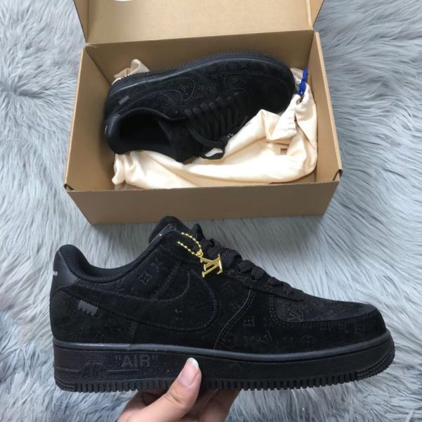 Black LV-branded sneakers with gold LV charm, shown near an open shoebox on a fluffy gray surface.