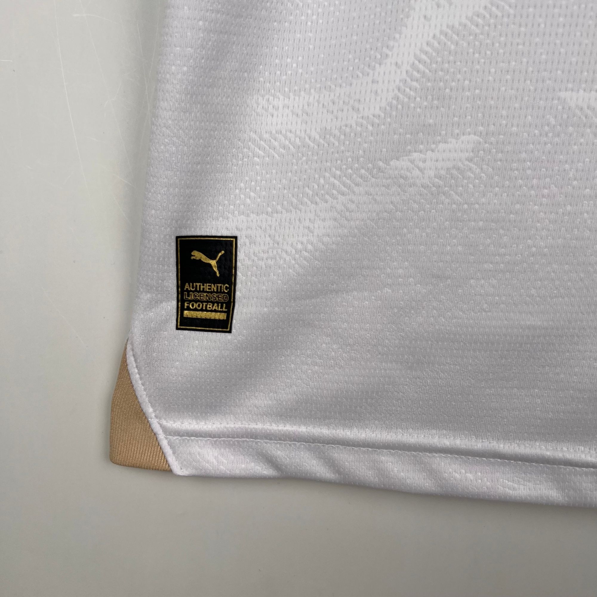 489ecca2_5dda8cd2-df60-4038-93a7-001c087b36f2 | AE JERSEY Close-up of light grey textured fabric with a small black-and-gold Puma label.