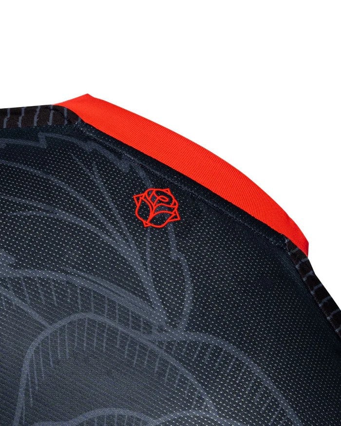4Krcacfe2oZrm5l | AE JERSEY Close-up of dark fabric with a dotted texture and a small red rose emblem near a red edge seam.