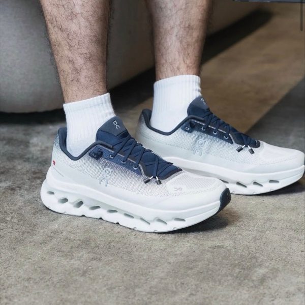 White and navy athletic sneakers with a chunky, hollowed sole and white socks, shown on a concrete floor.