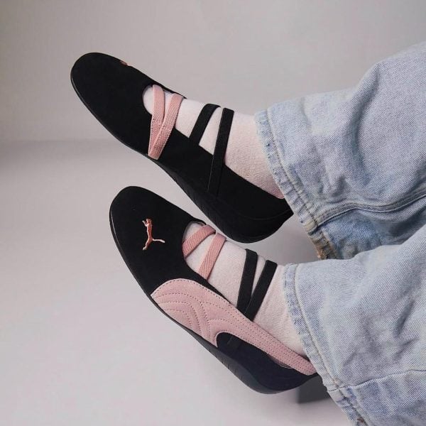 Black and pink sneakers with pink suede accents and striped straps, worn with light-pink socks and jeans. (Informative image of footwear)